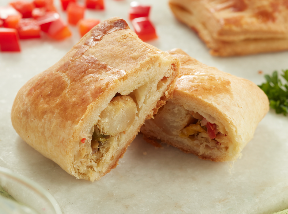Sauteed codfish with peppers wrapped in a buttery golden puff pastry on a marble table. 
